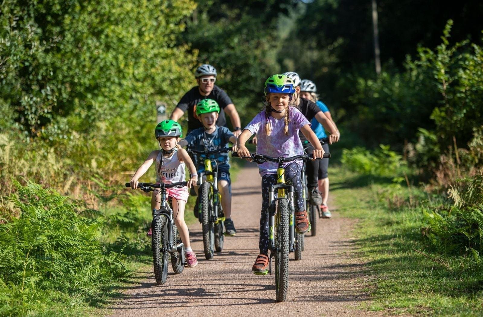 Family cycling towards camera smiling led by older girl and younger girl.