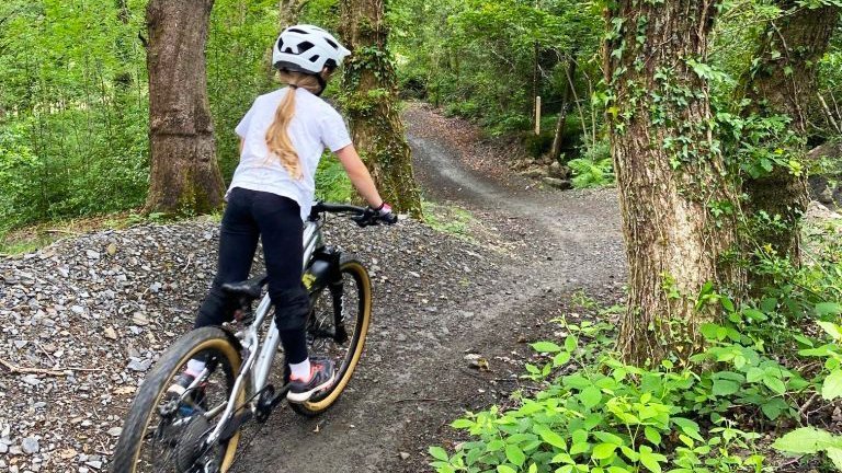 Photo of young girl riding a mountain bike on the gravel Dare Valley Family Gravity Bike Park trail through woodlands