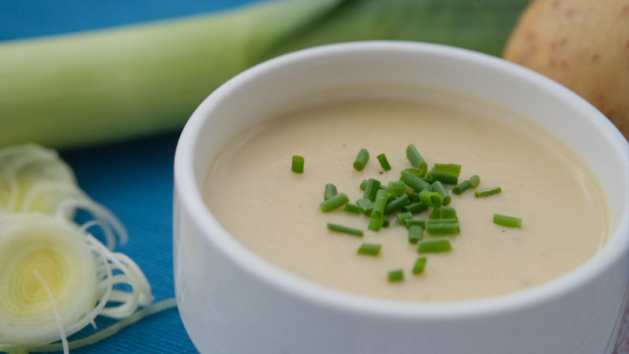 Photo of bowl of leek and potato soup with whole leeks and potatoes in the background