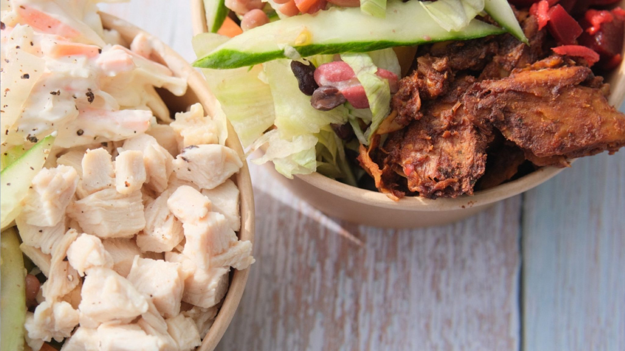 Photo of two cardboard bowls of salad, one with chicken and one with vegan pulled soya