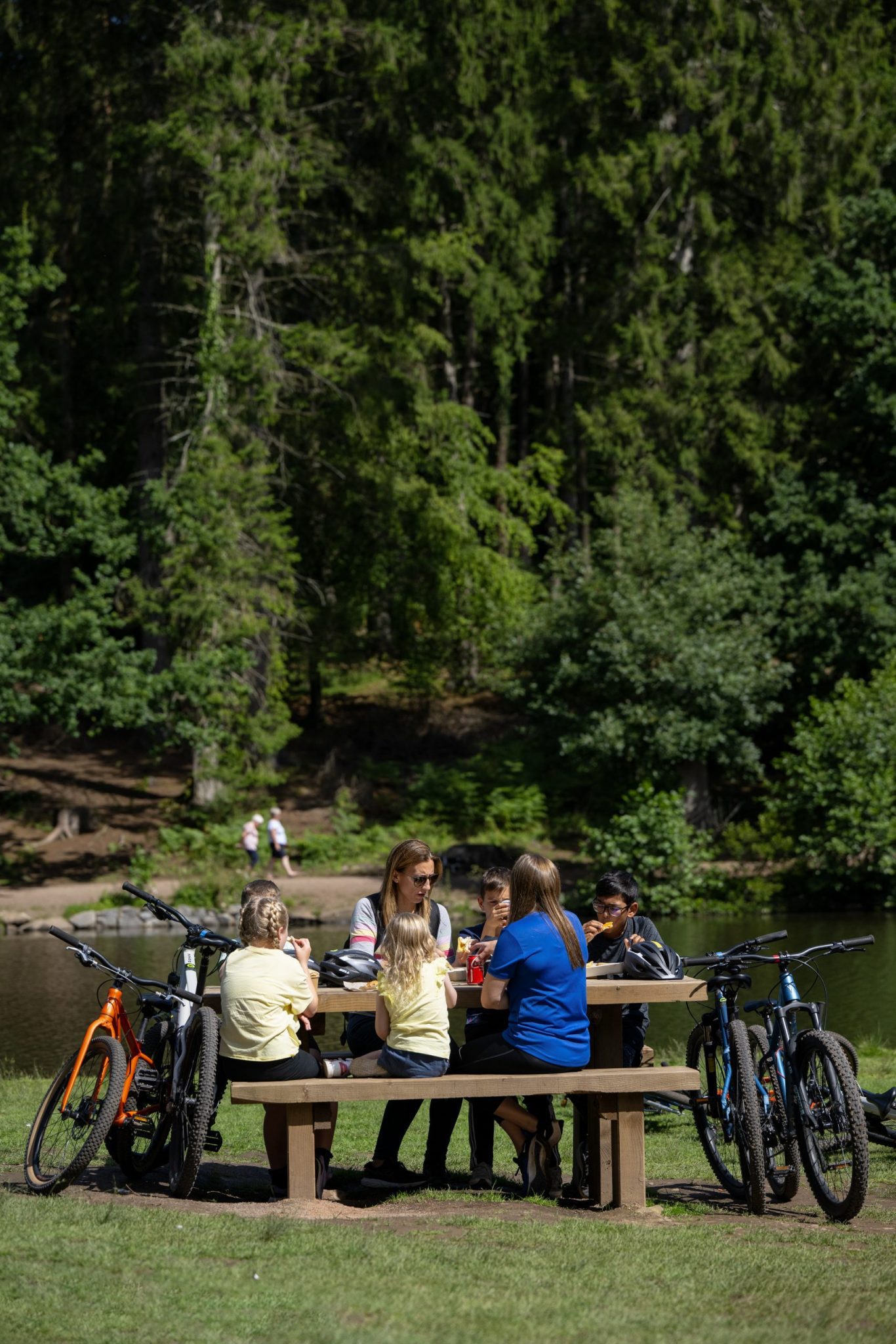Family sat at picnic bench next to lake with bikes propped up at either end.