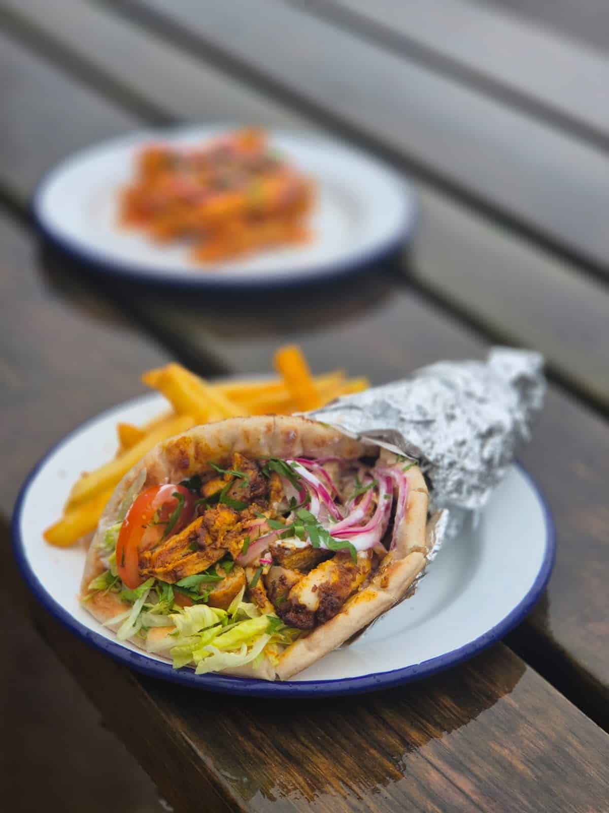 A chicken wrap filled with fresh lettuce, onion, tomato and spiced chicken with a side of fries