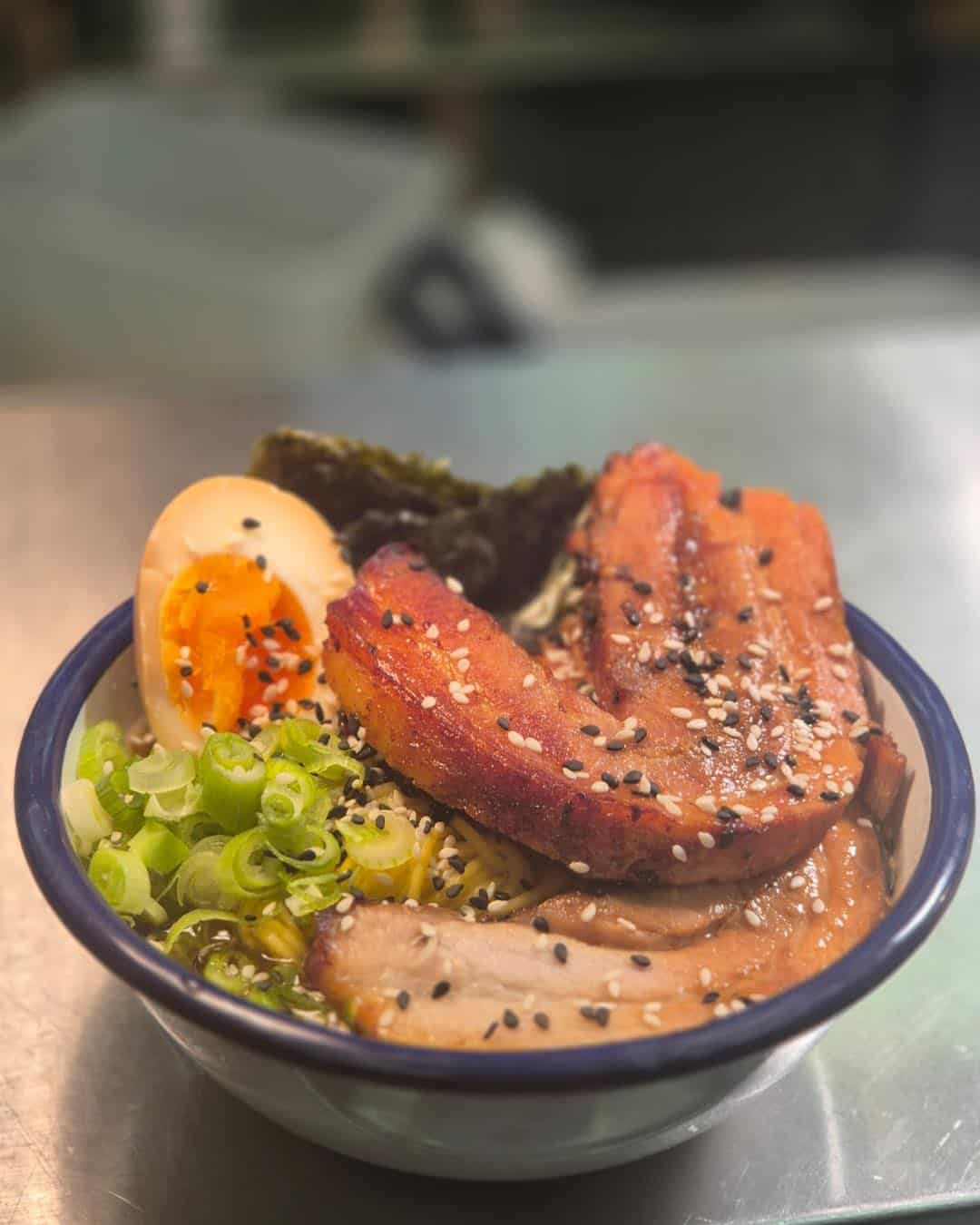 A bowl of ramen  topped with meat, egg, seaweed and spring onions