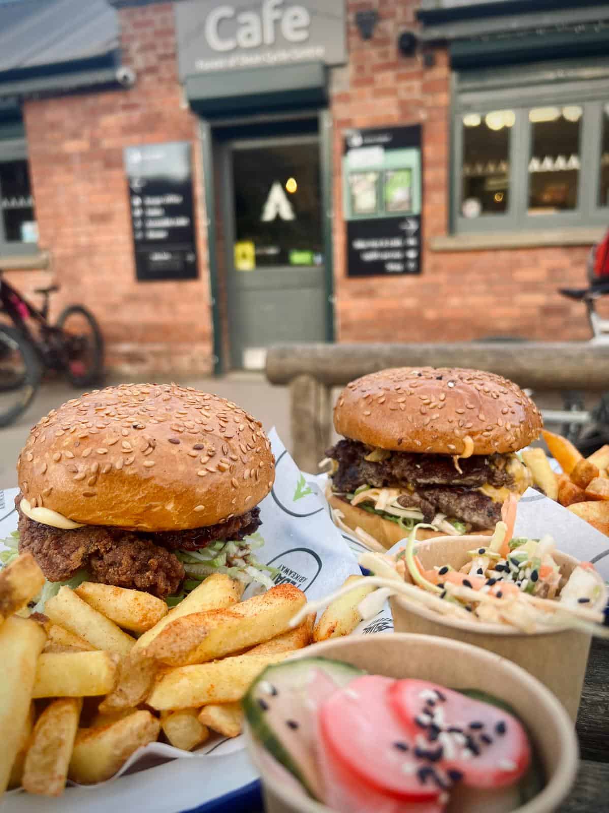 Two burgers, one beef, one chicken, with fries and sides of Korean slaw, photo taken in front of the Pedalabikeaway Cafe