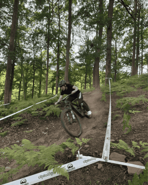 A woman on a mountain bike is riding downhill in a forest between race tape