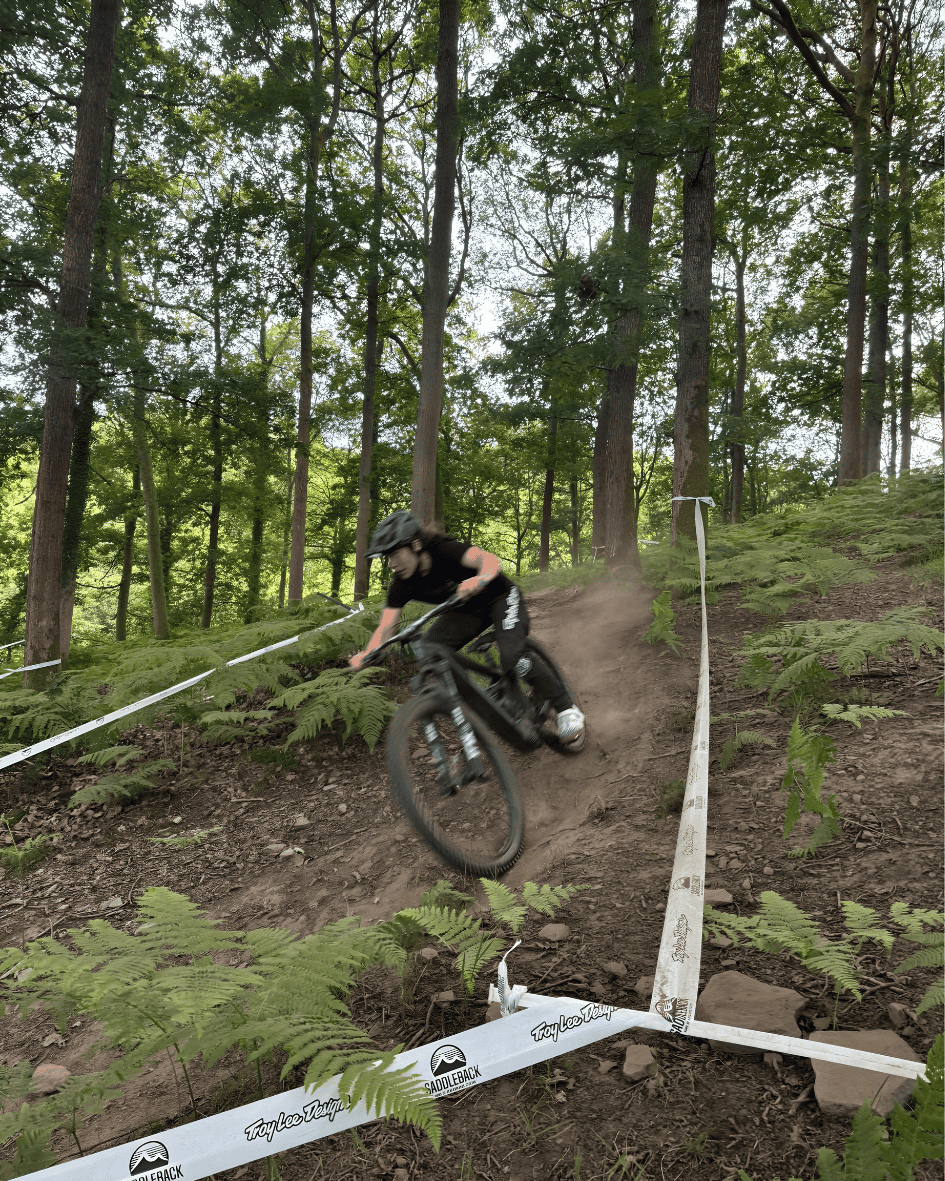 A woman on a mountain bike is riding downhill in a forest between race tape