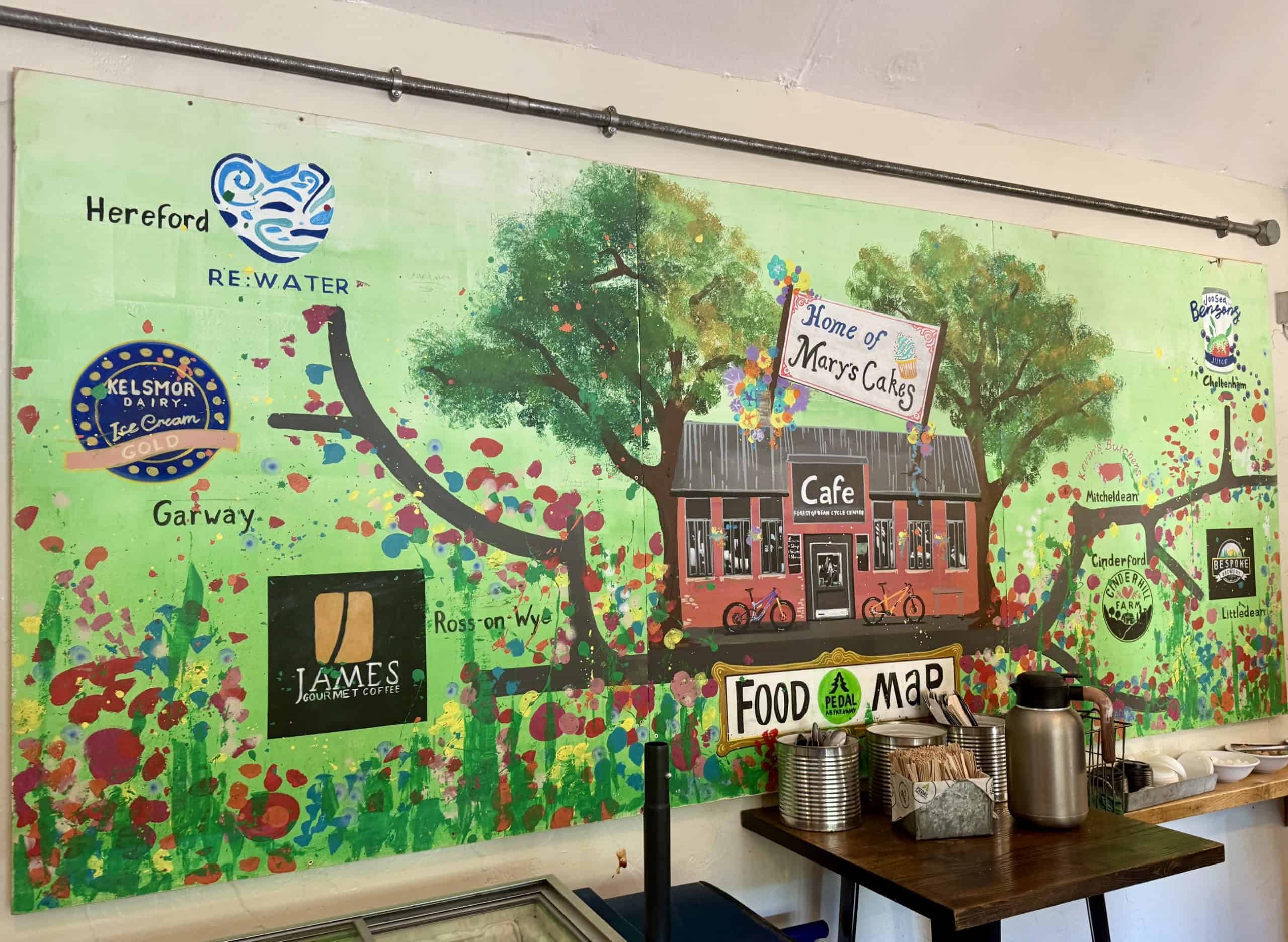 A painting done by one of our staff showing our cafe with a tree behind, the branches are a map to all our local suppliers, with each supplier named with their logo and location.